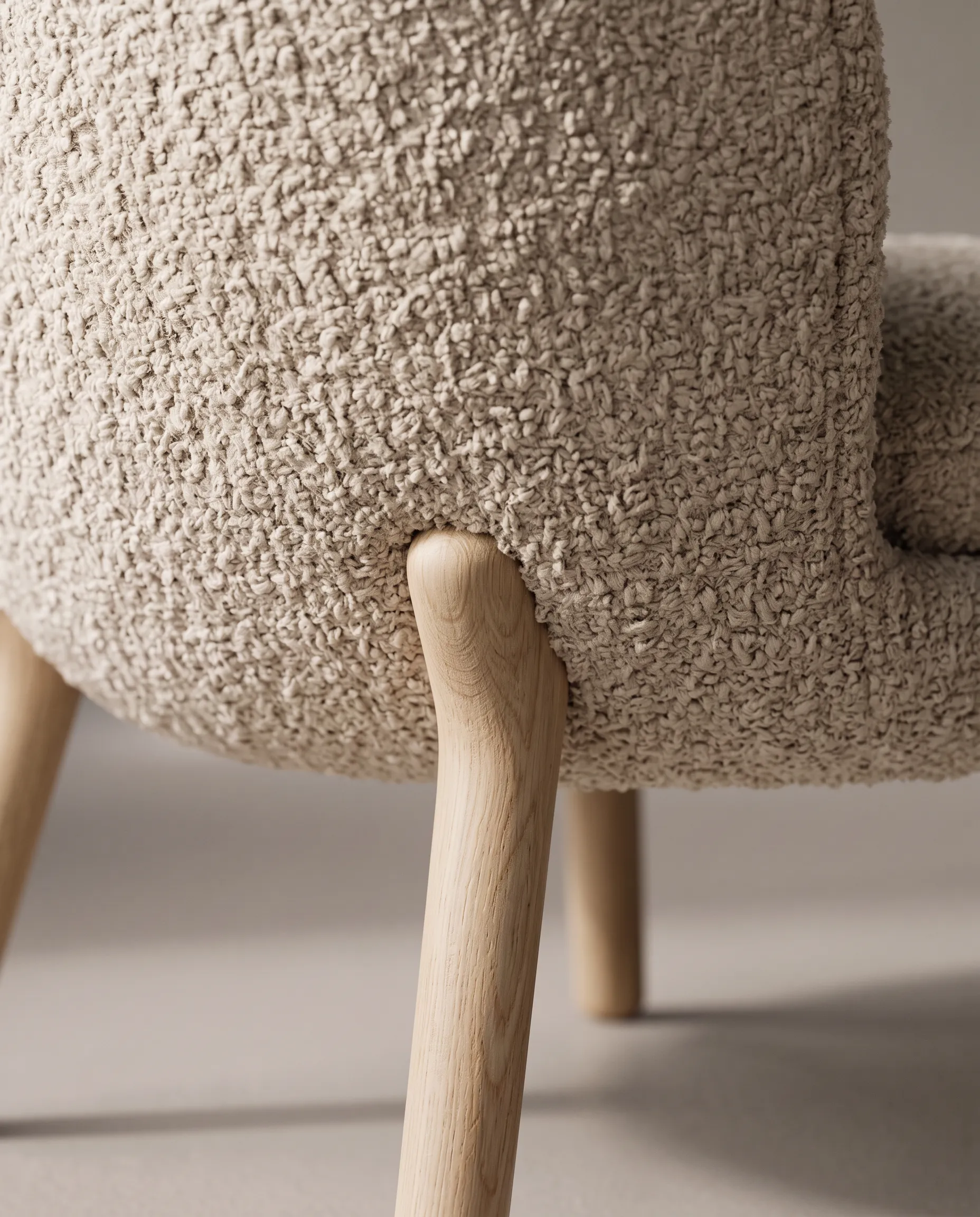Close view of oatmeal boucle meeting an oak chair leg