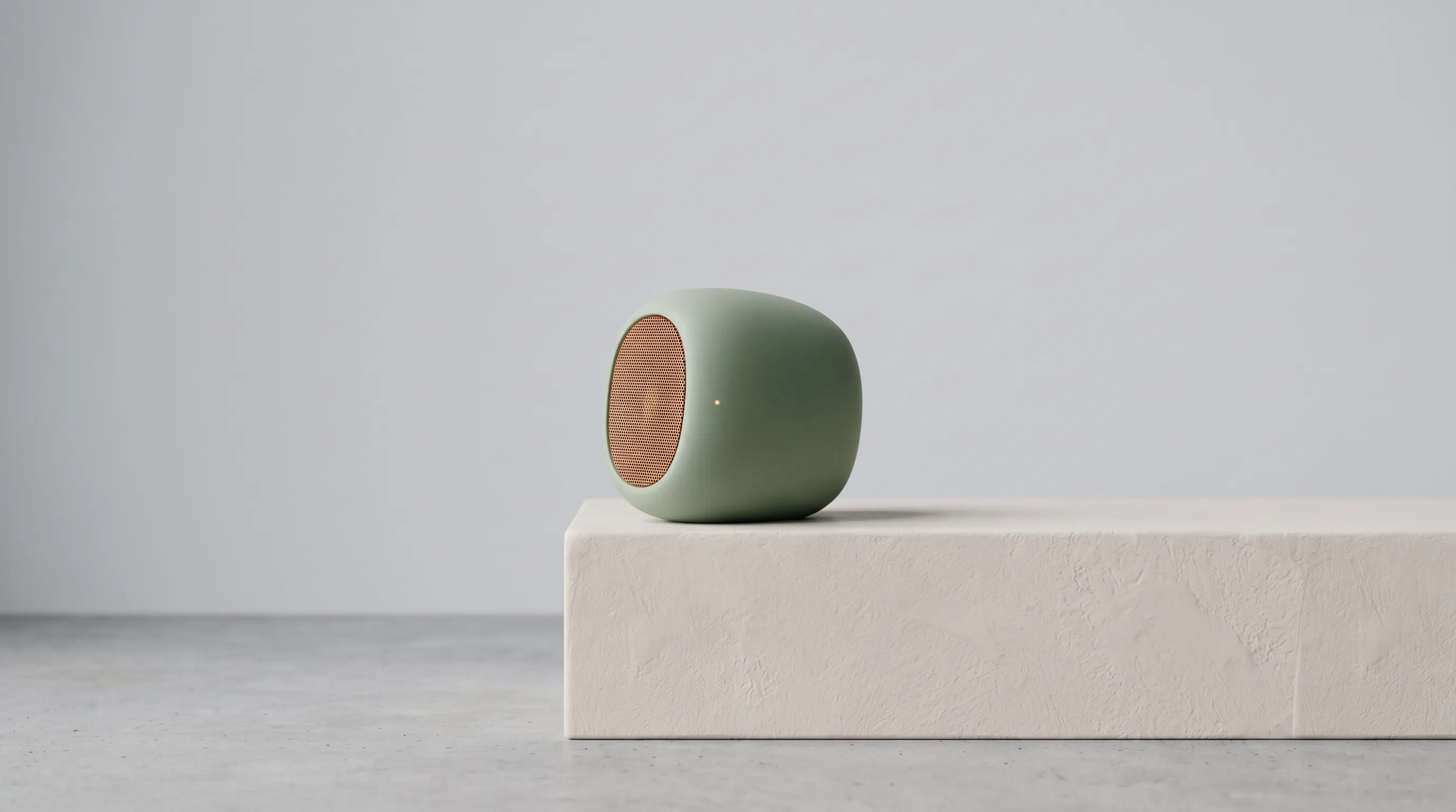 Sage pebble speaker on a plaster plinth in a gray studio
